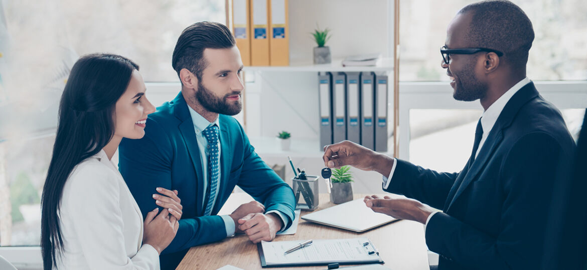 Side view portrait of couple is embracing, getting a key from their future apartment from a broker, and signing contract, all are dressed in formal outfits, sitting in workplace, workstation