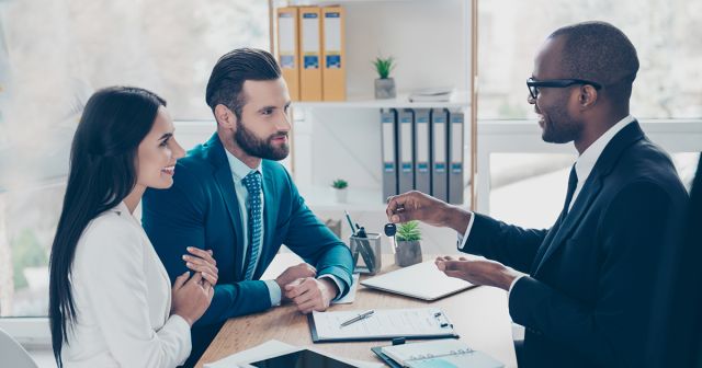 Side view portrait of couple is embracing, getting a key from their future apartment from a broker, and signing contract, all are dressed in formal outfits, sitting in workplace, workstation